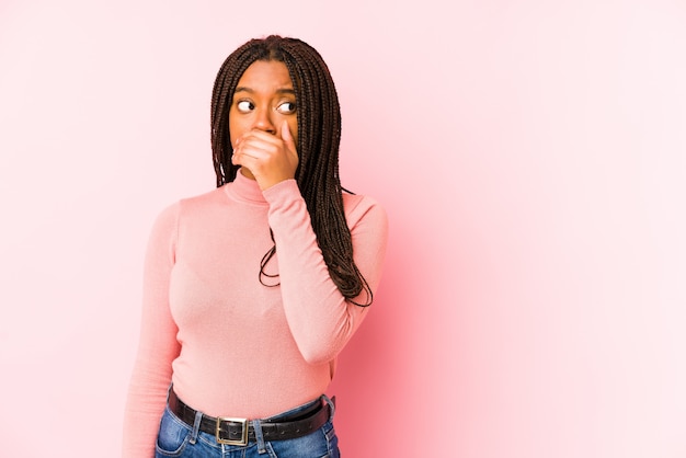 Junge Afroamerikanerfrau lokalisiert auf einem durchdachten Schauen der rosa Wand zu einem Kopienraumbedeckungsmund mit der Hand.