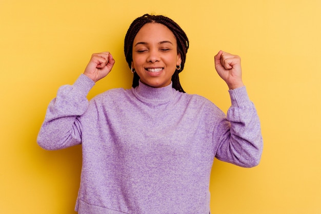 Junge Afroamerikanerfrau lokalisiert auf Gelb, das einen Sieg, Leidenschaft und Begeisterung, glücklichen Ausdruck feiert.