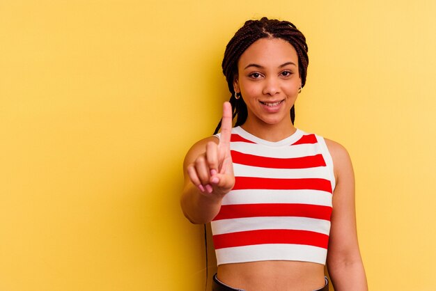 Junge Afroamerikanerfrau lokalisiert auf Gelb, das Nummer eins mit Finger zeigt.