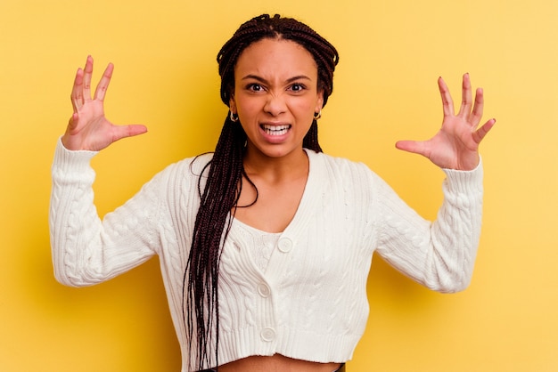 Junge Afroamerikanerfrau lokalisiert auf gelber Wand, die mit Wut schreit