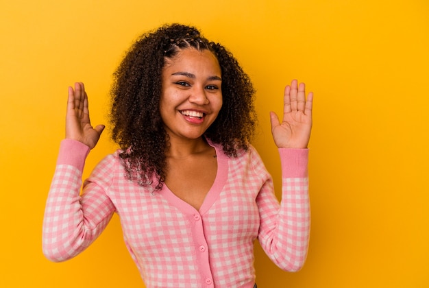 Junge Afroamerikanerfrau lokalisiert auf gelber Wand freudig viel lachend