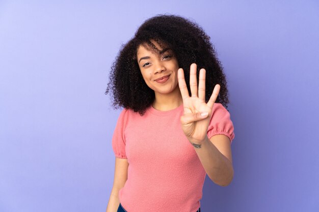 Junge Afroamerikanerfrau lokalisiert auf lila Wand glücklich und zählt vier mit den Fingern
