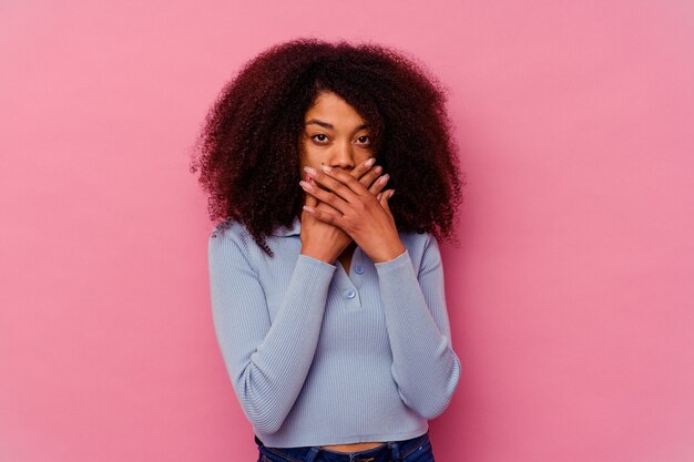 Junge Afroamerikanerfrau lokalisiert auf rosa geschocktem bedeckendem Mund mit Händen.