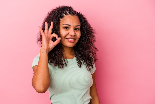 Junge Afroamerikanerfrau lokalisiert auf rosa Hintergrund fröhlich und zuversichtlich, ok Geste zeigend.
