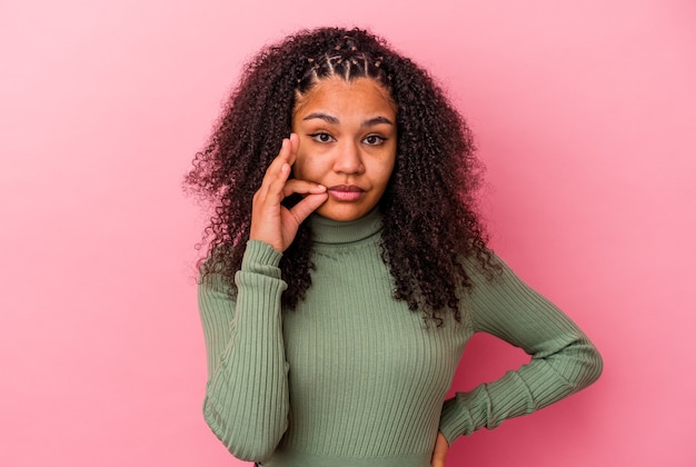 Junge Afroamerikanerfrau lokalisiert auf rosa Wand mit Fingern auf den Lippen, die ein Geheimnis halten.