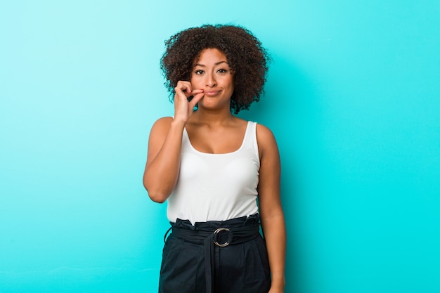 Junge Afroamerikanerfrau mit den Fingern auf den Lippen, die ein Geheimnis halten.