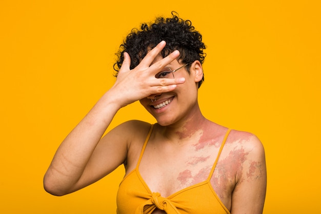 Junge Afroamerikanerfrau mit Hautgeburtszeichenblinken an der Kamera durch Finger