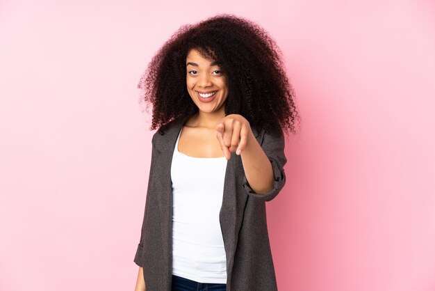 Junge Afroamerikanerfrau über isolierter Wand überrascht und nach vorne zeigend