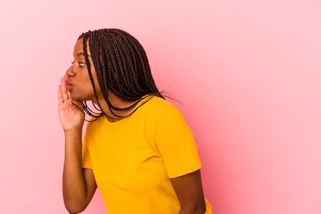 Junge Afroamerikanerin, die auf rosafarbenem Hintergrund isoliert ist, sagt eine geheime heiße Bremsnachricht und schaut beiseite