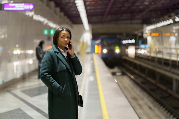 Junge Afroamerikanerin, die beim Warten auf den Zug am U-Bahnsteig Handy telefoniert