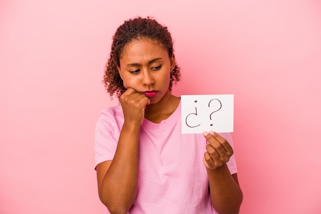 Foto junge afroamerikanerin, die ein frageschild auf rosafarbenem hintergrund hält