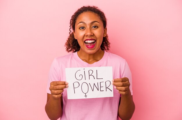 Junge Afroamerikanerin, die ein Girl-Power-Plakat auf rosafarbenem Hintergrund hält