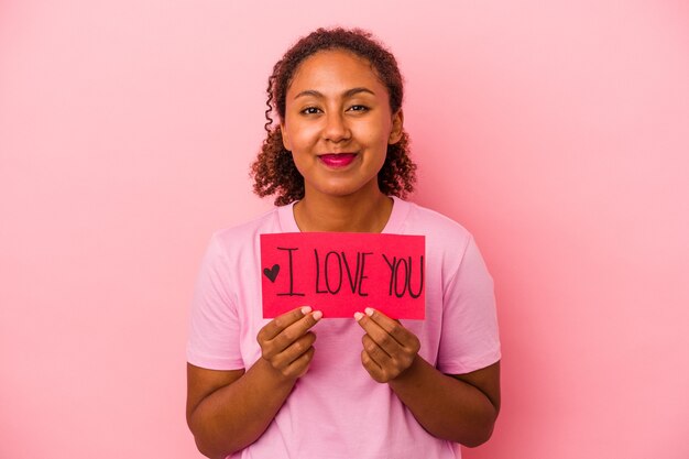 Junge Afroamerikanerin, die ein "Ich liebe dich"-Plakat auf rosafarbenem Hintergrund hält