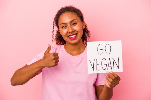 Junge Afroamerikanerin, die ein veganes Plakat hält, das auf rosa Hintergrund isoliert ist