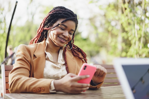 Junge Afroamerikanerin, die im Straßencafé sitzt und Smartphone in den Händen hält