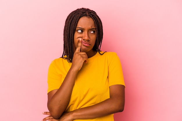 Junge Afroamerikanerin einzeln auf rosafarbenem Hintergrund, die seitlich mit zweifelhaftem und skeptischem Ausdruck schaut.