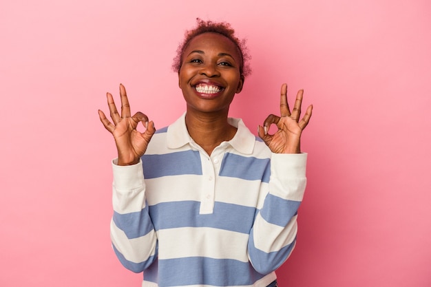Junge Afroamerikanerin einzeln auf rosafarbenem Hintergrund fröhlich und selbstbewusst, die eine gute Geste zeigt.