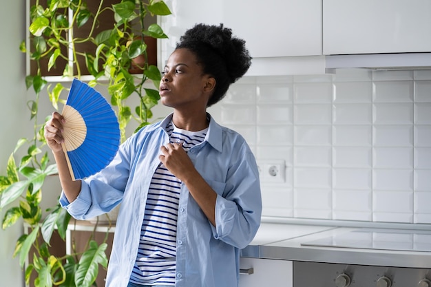 Junge Afroamerikanerin in blauem Hemd, die sich wegen des heißen Wetters mit Handfächern auffächert