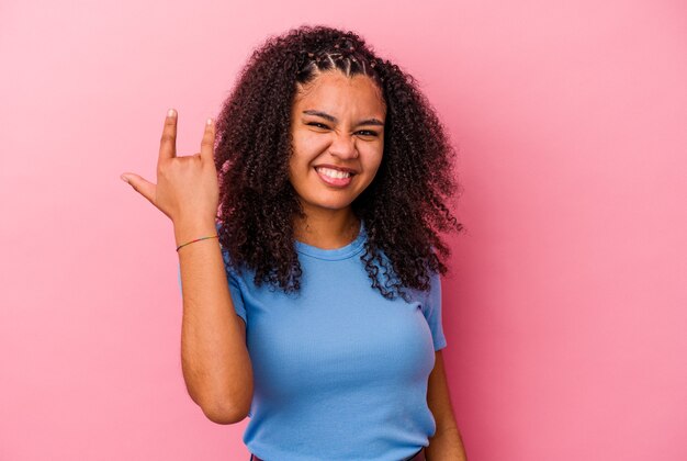 Junge Afroamerikanerin isoliert auf rosa Hintergrund, die Rockgeste mit den Fingern zeigt