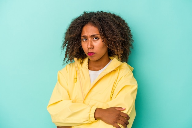 Junge Afroamerikanerin mit lockigem Haar isoliert auf blauem Hintergrund misstrauisch, unsicher, untersucht Sie.