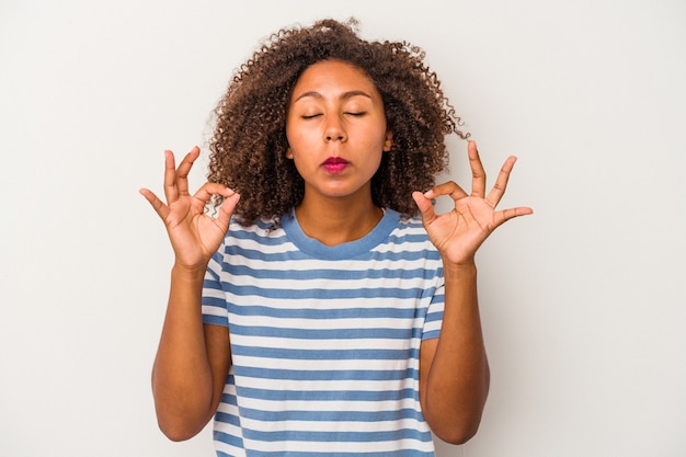 Junge Afroamerikanerin mit lockigem Haar, isoliert auf weißem Hintergrund, entspannt sich nach einem harten Arbeitstag, sie führt Yoga durch.