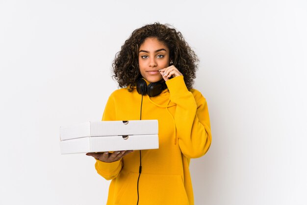 Junge Afroamerikanerstudentenfrau, die Pizzas mit den Fingern auf den Lippen halten ein Geheimnis hält.
