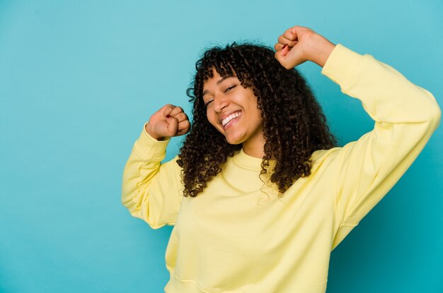 Junge afroamerikanische Afro-Frau isoliert, die einen besonderen Tag feiert, springt und Arme mit Energie hebt.