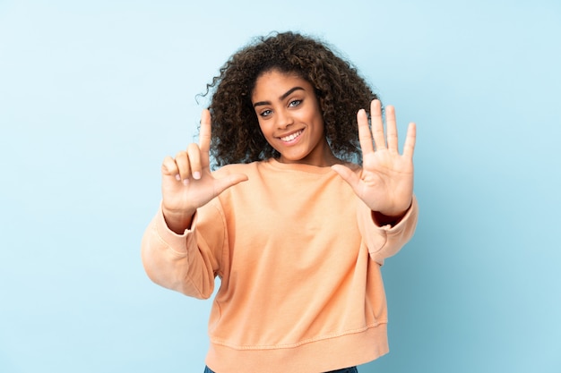 Junge afroamerikanische Frau auf blauer Wand, die sieben mit den Fingern zählt