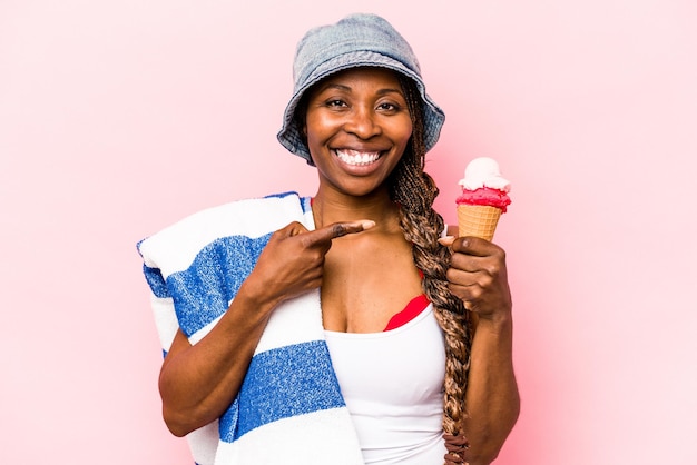 Junge afroamerikanische Frau, die an den Strand geht und ein Eis isoliert auf rosa Hintergrund hält