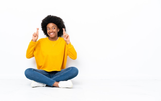 Junge afroamerikanische Frau, die auf dem Boden mit den Fingern kreuzend sitzt