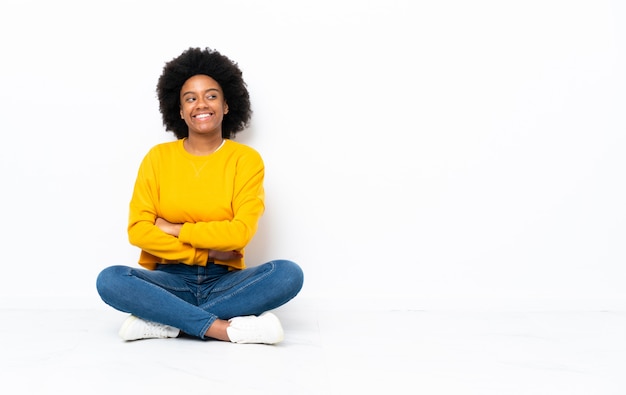 Junge afroamerikanische Frau, die auf dem Boden mit verschränkten Armen und glücklich sitzt