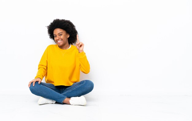 Junge afroamerikanische Frau, die auf dem Boden sitzt und einen Finger im Zeichen des Besten zeigt und hebt