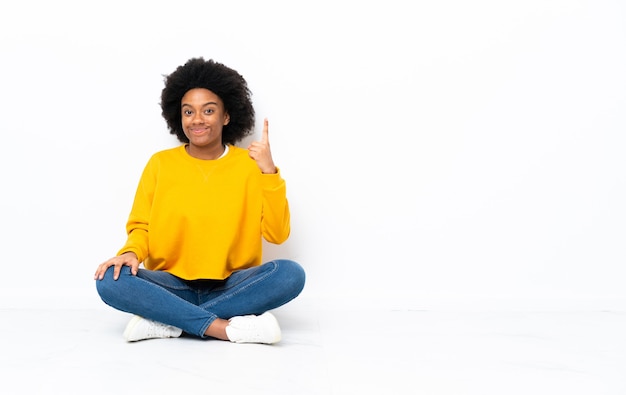 Junge afroamerikanische Frau, die auf dem Boden sitzt und mit dem Zeigefinger eine große Idee zeigt