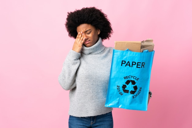 Junge afroamerikanische Frau, die einen Recyclingbeutel lokalisiert auf bunter Wand mit Kopfschmerzen hält