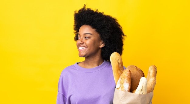 Junge afroamerikanische Frau, die etwas Brot auf der gelben Wand kaufenden Seite kauft