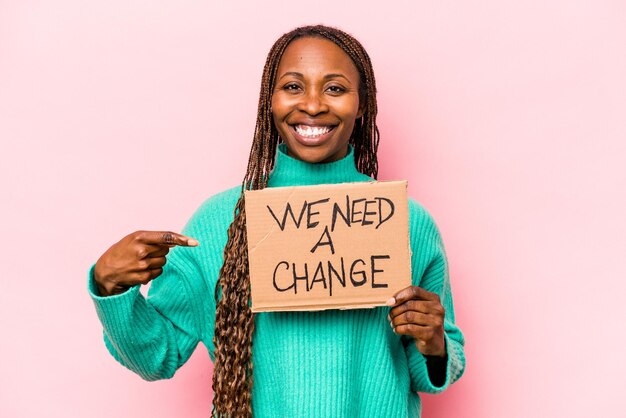 Junge afroamerikanische Frau, die hält, wir brauchen ein Änderungsplakat, das auf rosafarbenem Hintergrund isoliert ist