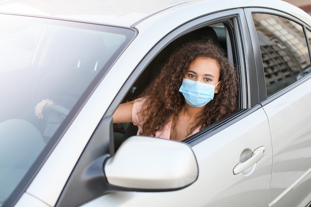 Junge afroamerikanische Frau, die medizinische Maske beim Sitzen im Auto trägt