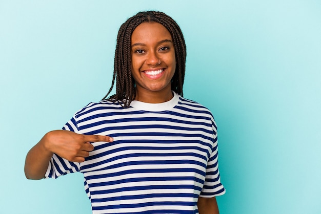 Junge afroamerikanische Frau einzeln auf blauem Hintergrund, die mit der Hand auf einen Hemdkopierraum zeigt, stolz und selbstbewusst
