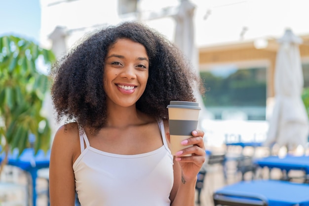 Junge afroamerikanische Frau im Freien, die mit einem glücklichen Gesichtsausdruck einen Take-Away-Kaffee hält