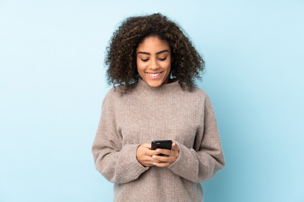 Junge afroamerikanische Frau isoliert auf Blau, das eine Nachricht mit dem Handy sendet