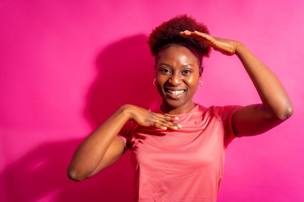 Junge afroamerikanische Frau, isoliert auf rosa Hintergrund, lächelt und tanzt im Studio