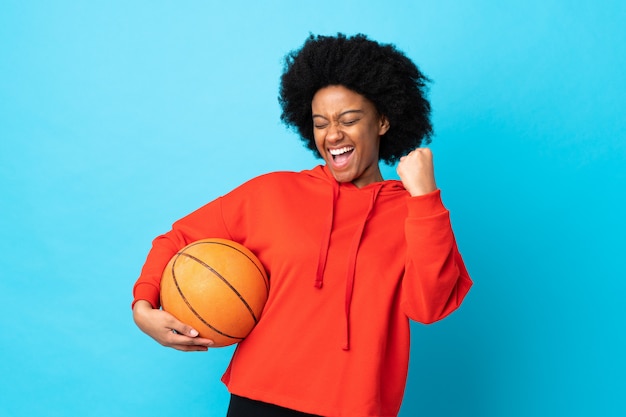 Junge afroamerikanische Frau lokalisiert auf blauer Wand, die Basketball spielt