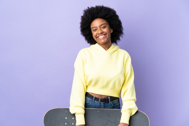 Junge afroamerikanische Frau lokalisiert auf lila Hintergrund mit einem Skate mit glücklichem Ausdruck