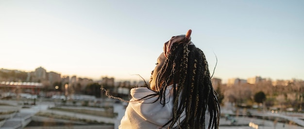 Junge afroamerikanische Frau mit Dreadlocks von hinten, die die Rückansicht der Stadt betrachtet