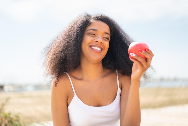 Junge afroamerikanische Frau mit einem Apfel im Freien mit fröhlichem Gesichtsausdruck