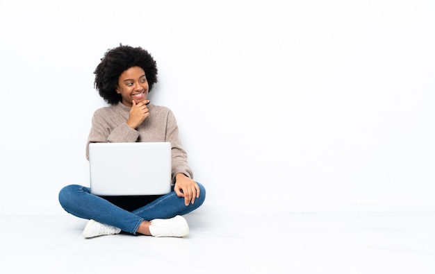 Junge afroamerikanische Frau mit einem Laptop, der auf dem Boden sitzt und zur Seite schaut