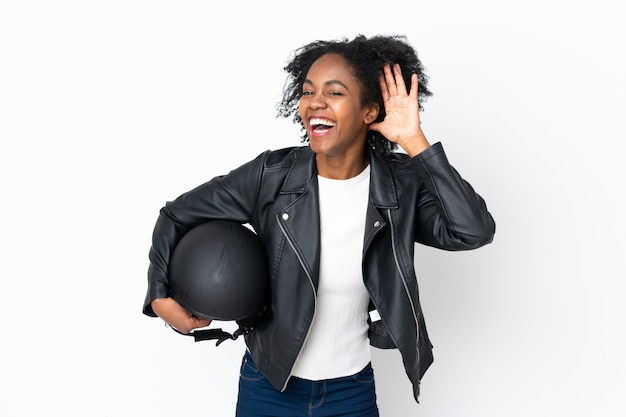 Junge afroamerikanische Frau mit einem Motorradhelm auf weißer Wand, die etwas hört