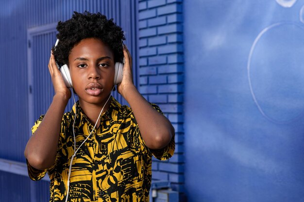 Junge afroamerikanische Frau mit kurzen Haaren und modernen Kleidern hört Musik mit Kopfhörern