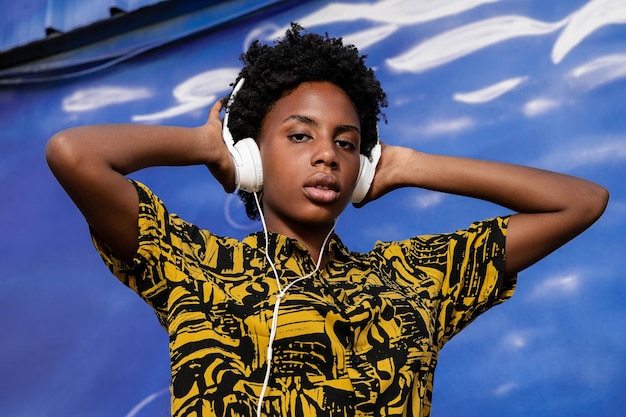Junge afroamerikanische Frau mit kurzen Haaren und modernen Kleidern hört Musik mit Kopfhörern