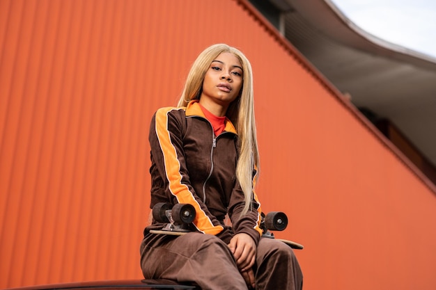 Junge afroamerikanische Frau mit langen blonden Haaren und Sportbekleidung auf orangefarbenem Hintergrund